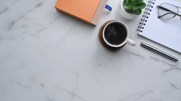 istock Top view coffee cup, notebook, eyeglasses and plant on marble background. 1337185755