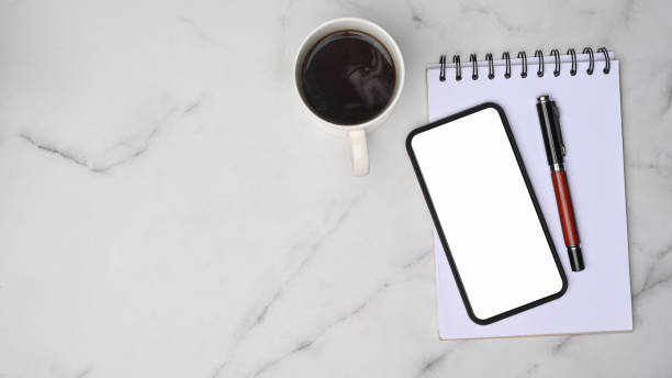 istock Top view mobile phone, coffee cup, pen and notepad on marble background. 1337186333