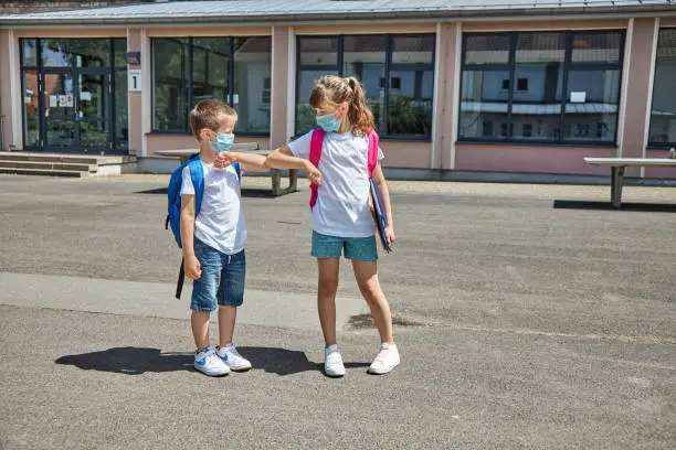A boy and a girl greet their elbows in masks in the school yard. New school year, back to school. Schoolchildren in a new reality.