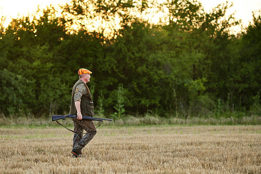 Hunter with rifle walking in rural field during hunting
