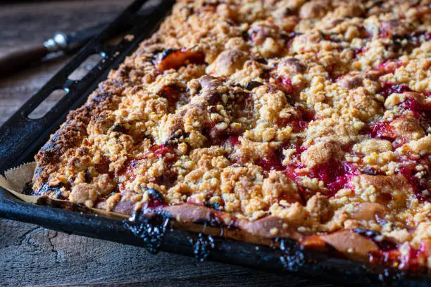 Closeup of a delicious Plum Crumble cake  on a baking tray. fresh and homemade baked and served on wooden and rustic table background