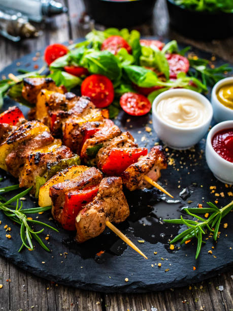 Shashlik - grilled meat and vegetables on stone plate on wooden table Shashlik - grilled meat and vegetables on stone plate on wooden table kebab stock pictures, royalty-free photos & images