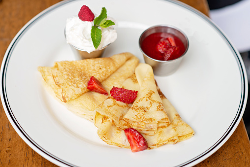 Delicious crepes with fresh strawberries, mint leaves and sour cream espuma. Breakfast at the restaurant. Soft selective focus.