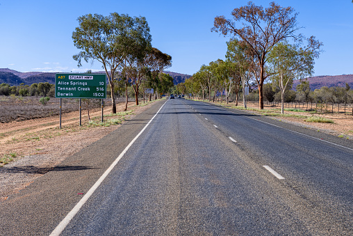 street sign keep an eye out for wildlife and drive with care showing images of an emu, kangaroo, iguana and echidna besides an asphalt road in Australia and a car with trailer
