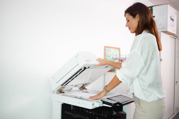 istock Female office clerk loading xerox with documents for copying 1337204453
