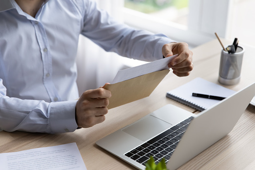 Hands of businessman opening envelope with white paper, taking out document for reading. Business leader, executive, CEO receiving letter, invitation, notification, postcard at workplace. Close up