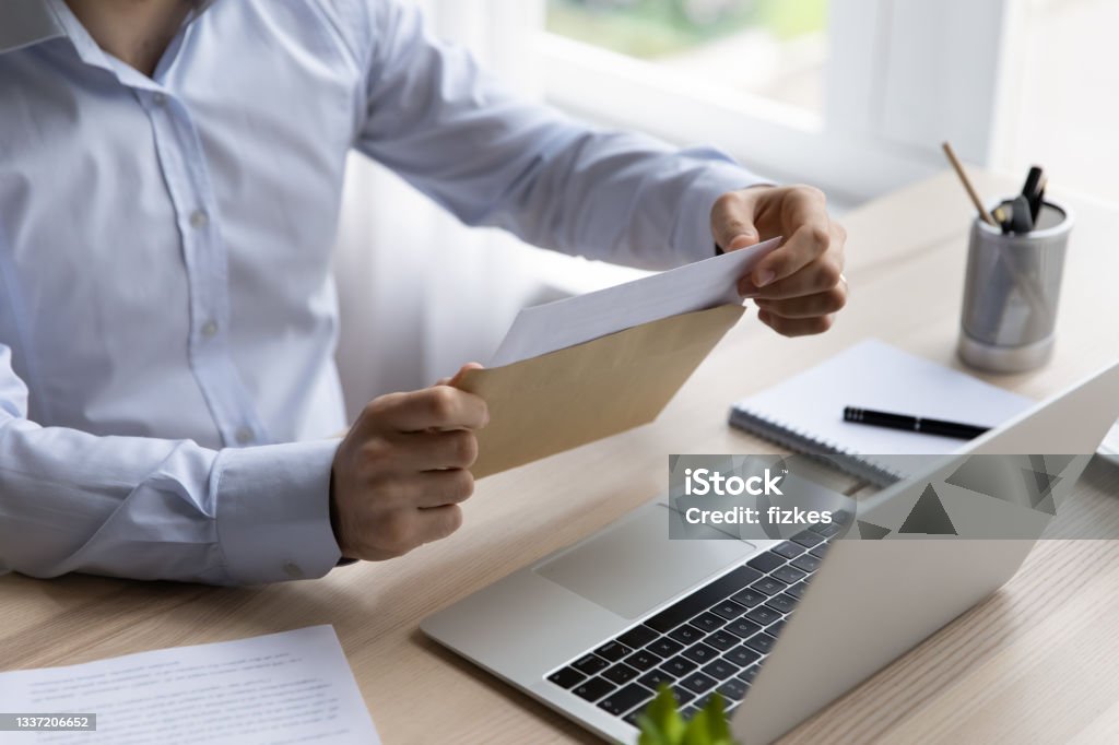 Hands of businessman opening envelope with white paper Hands of businessman opening envelope with white paper, taking out document for reading. Business leader, executive, CEO receiving letter, invitation, notification, postcard at workplace. Close up Letter - Document Stock Photo