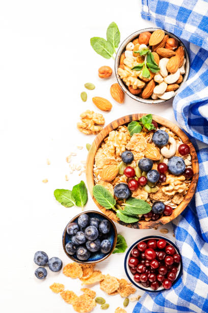 Muesli bowl and organic ingredients for healthy breakfast. Granola, nuts, blueberry, cranberry, oatmeal, greek yoghurt, whole grain flakes on white table