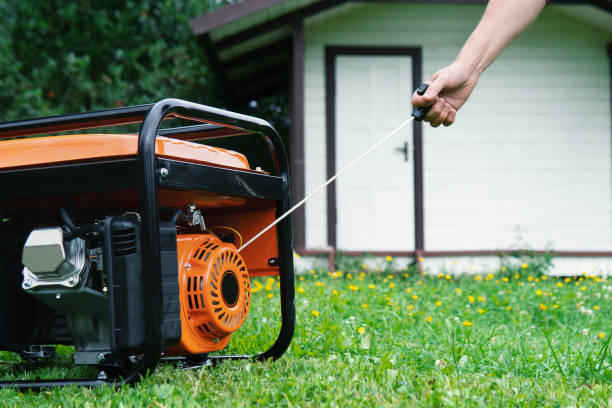 Hand starts a portable electric generator in front of a summer house in summer stock photo