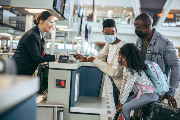 Traveler family at airport check-in counter Travelers at check-in counter with airlines staff during pandemic. African family checking in at airport,  giving passport to airline attendant. check in person stock pictures, royalty-free photos & images