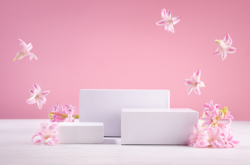 Set of tree white podiums for presentation cosmetics produce with  flying fresh spring flowers  on pastel pink background.