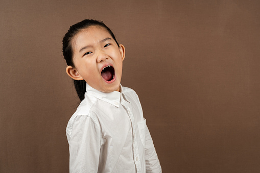 Little girl yawning on brown background