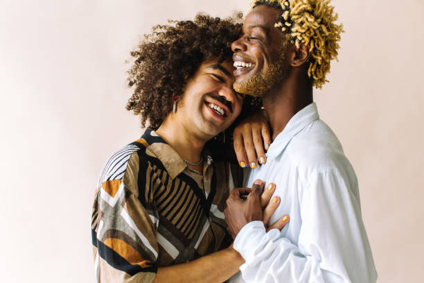 Cheerful gay couple embracing each other in a studio Cheerful young gay couple standing together in a studio. Two affectionate male lovers smiling cheerfully while embracing each other against a studio background. Young gay coupe being romantic. lgbtqi rights stock pictures, royalty-free photos & images