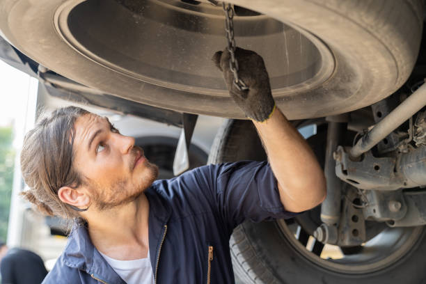 istock Male car mechanic worker working using wrench tool for repair, maintenance underneath lifted car. Mechanic vehicle service checking under car in garage. Auto car repair service, maintenance concept 1337219229
