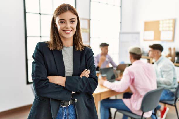 młoda latynoska bizneswoman uśmiechająca się szczęśliwie stojąc ze skrzyżowanymi rękami gestem w biurze podczas spotkania biznesowego. - businessman business arms crossed business person zdjęcia i obrazy z banku zdjęć