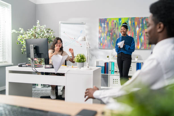 istock Co-workers elegantly dressed sitting in the office in the corporation, cheerful work, funny atmosphere, friends throwing at each other folded paper planes, joking, laughing, business in the company 1337221216