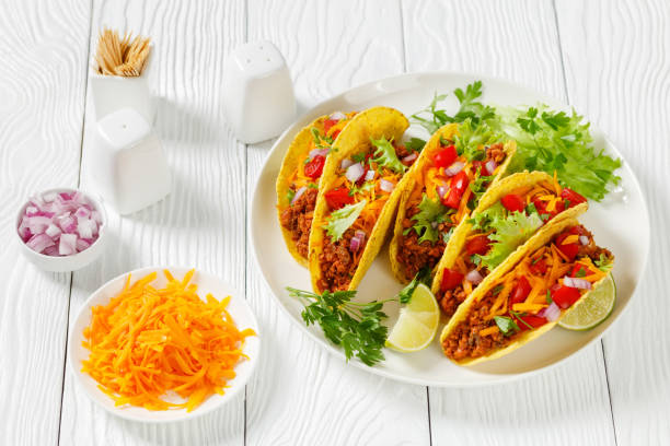 istock Ground Beef Tacos with shredded cheddar cheese, fresh lettuce, tomato, onion on a white plate with lime wedges, horizontal view from above, mexican cuisine 1337222134