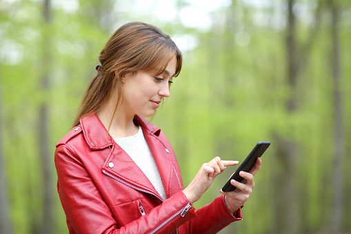 Woman in red checking smart phone in a forest