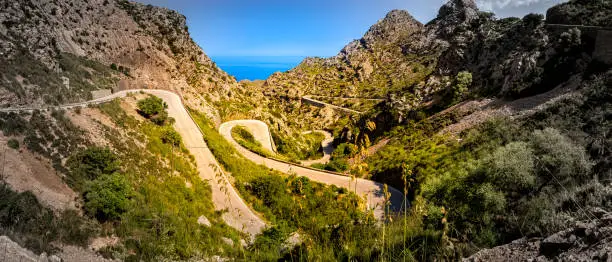 Wide angle panorama of balearic serpentine route MA-2141 winding down to sa calobra through a valley in the area of coll dels reis in the famous sierra de tramuntana mountain range, mallorca, spain