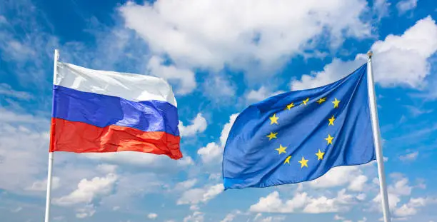 Waving russian and European Union flags against blue sky background. Partnership and cooperation concept.