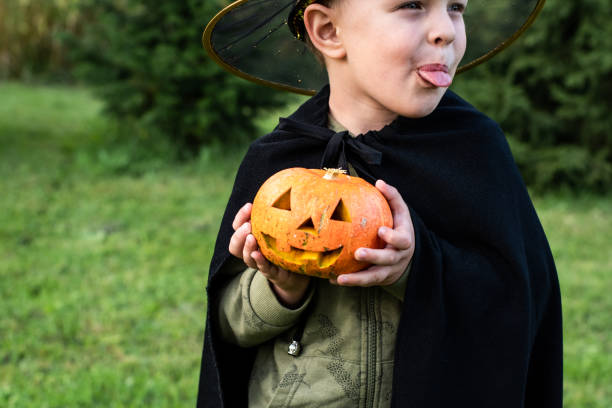 A little boy in a wizard costume holds a jack'o'lantern pumpkin for Halloween. Happy Halloween. A child in a fancy dress with a pumpkin in the garden