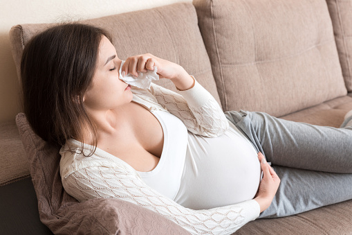 Mujer embarazada enferma que se sopla la nariz en el tejido en casa Concepto de atención médica milenaria saludable photo