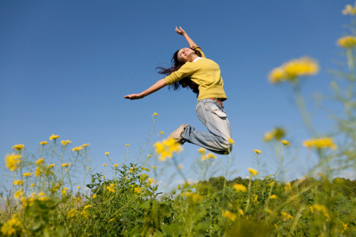 Happy and beautiful young girl jumping high in a summer field