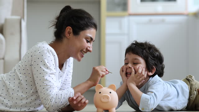 Indian mother her little son drop coins into piggy bank