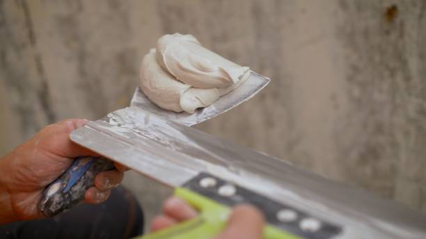 istock Builder using a trowel to add plaster. Plastering wall with putty-knife, close up image. Fixing wall surface and preparation for painting. Close-up of a spatula with a construction putty 1337233080