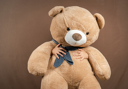 Child Holding a Big Teddy Bear to Block Himself on Brown Background