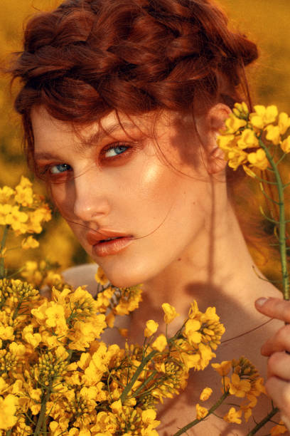 portrait de jeune mannequin aux cheveux de gingembre et aux yeux bleus dans un champ de colza jaune - ethnic editorial make up colors photos et images de collection