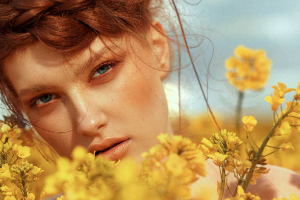 portrait de jeune mannequin aux cheveux de gingembre et aux yeux bleus dans un champ de colza jaune - ethnic editorial make up colors photos et images de collection