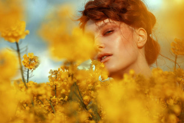 young fashion model portrait with ginger hair and blue eyes in yellow rapeseed field - fotos de boho imagens e fotografias de stock