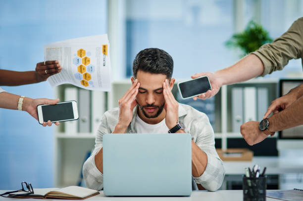 Shot of a young man experiencing a headache at work while being overwhelmed stock photo