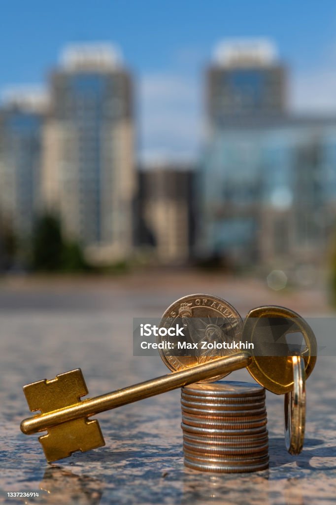 Golden key and column of american coins on the background of modern buildings Venture Capital Stock Photo