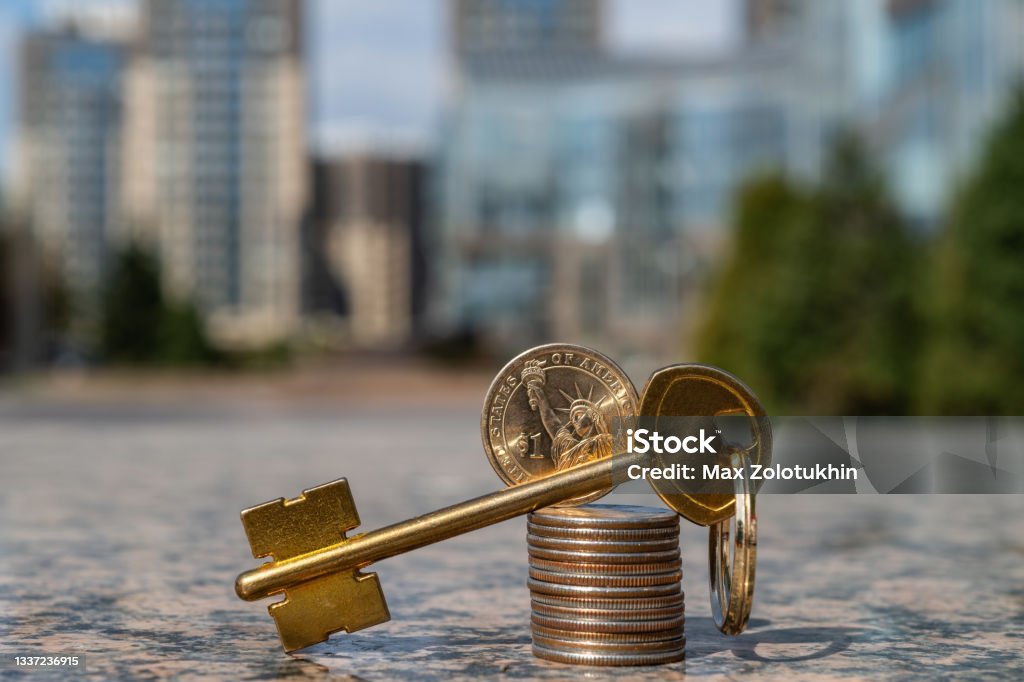 Golden key and column of american coins on the background of modern buildings Apartment Stock Photo