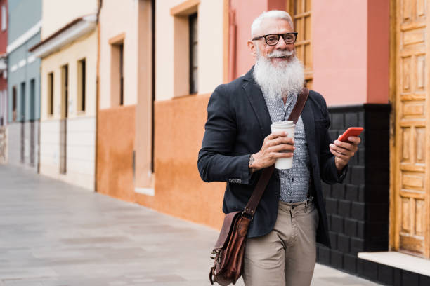 istock Hipster senior business man using smartphone and drinks coffee while walking to work - Focus on face 1337240135
