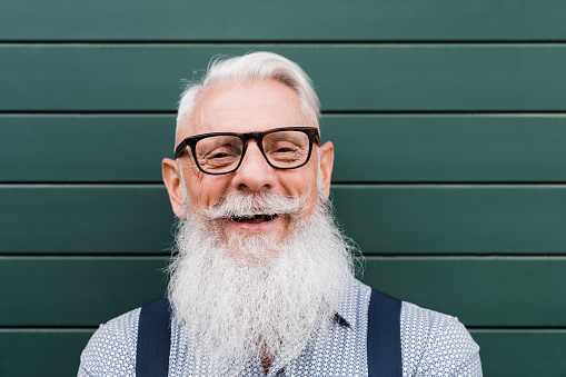 Happy hipster senior man smiling on camera with green background - Focus on face