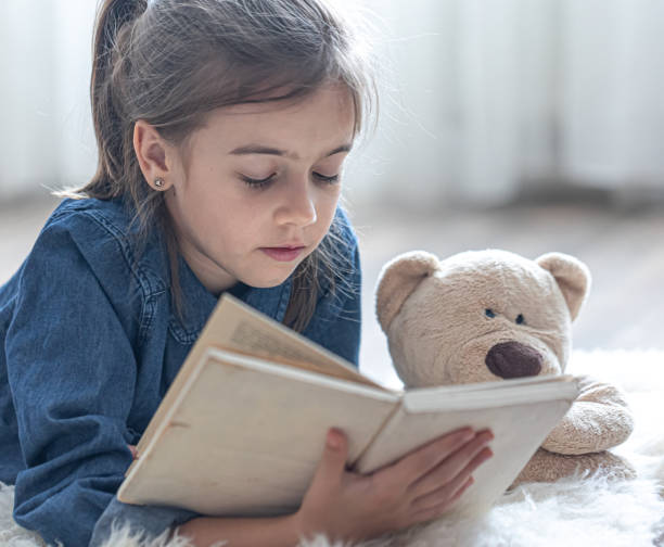 istock Little girl reads a book with a teddy bear. 1337242390