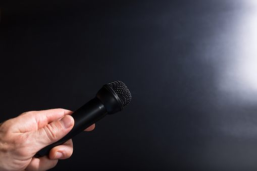 Male hand holding black microphone and taking interview on black background with copy space.