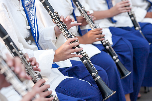 Thai youth orchestra in North Thai traditional clothing performs in a traditional music festival. Close-up youth musicians hand playing clarinet.