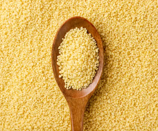 Couscous in a spoon on the background of cereals close-up. The view from top