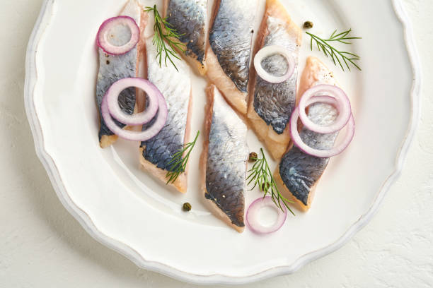 istock Salted herring with spice, herbs and onion on white plate on light stone background with copy space. Marinated sliced fish. Food with healthy unsaturated fats, flat lay 1337249551