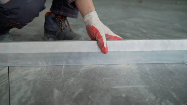 A worker checks the laid tiles on the floor. The foreman checks the level of the laid tiles on the floor. A worker checks the laid tiles on the floor. el capataz verifica el nivel de las baldosas colocadas en el piso. un trabajador en un uniforme de construcción verifica el nivel de la superficie en las baldosas de gres porcelánico mientras coloca el piso en un edificio en construcción.