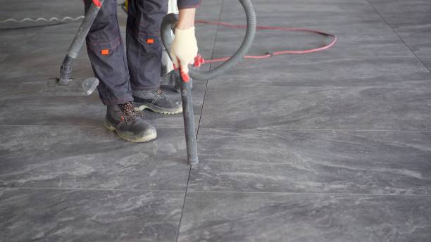 istock Worker cleans seams between tiles using a vacuum cleaner. Tile master, vacuums the floor to prepare for trowelling. A worker vacuums the ceramic tile floor 1337250024