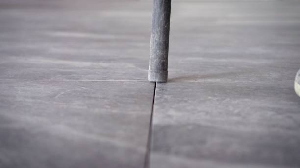 istock Worker cleans seams between tiles using a vacuum cleaner. Tile master, vacuums the floor to prepare for trowelling. A worker vacuums the ceramic tile floor 1337250033