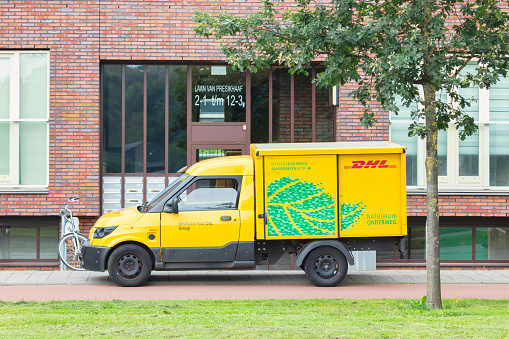 Arnhem, The Netherlands - July 21, 2021: Electric DHL postal courier car in front of an apartment building in Arnhem, The Netherlands