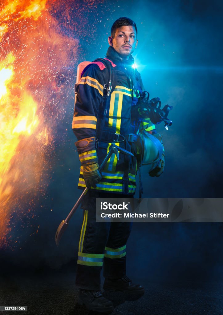 Firefighter in front of fire and blue light Firefighters control and put out fires and respond to emergencies involving life, property, or the environment. Firefighter Stock Photo