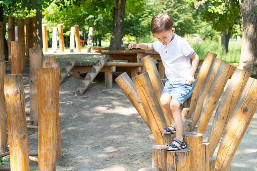 Children's obstacle course on a modern playground. Kid crossing a wooden bridge using his body balance. Development of the child's agility and courage.