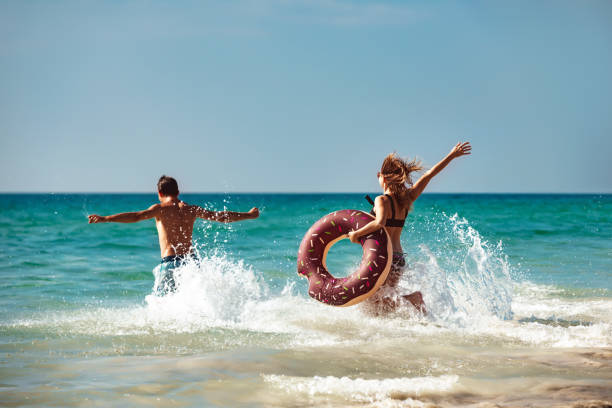 Happy young couple with inflatable donut at sea beach stock photo